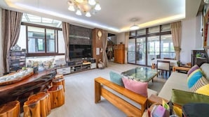 A spacious living room with a large TV, wooden furniture, and large windows.