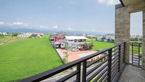 A balcony with a view of a green field and a red building.
