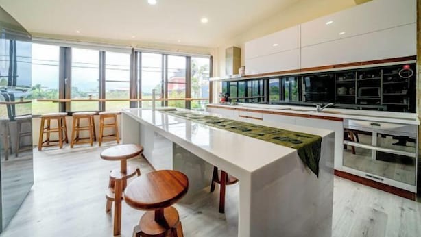 A modern kitchen with a large island, bar stools, and a view of the outdoors.