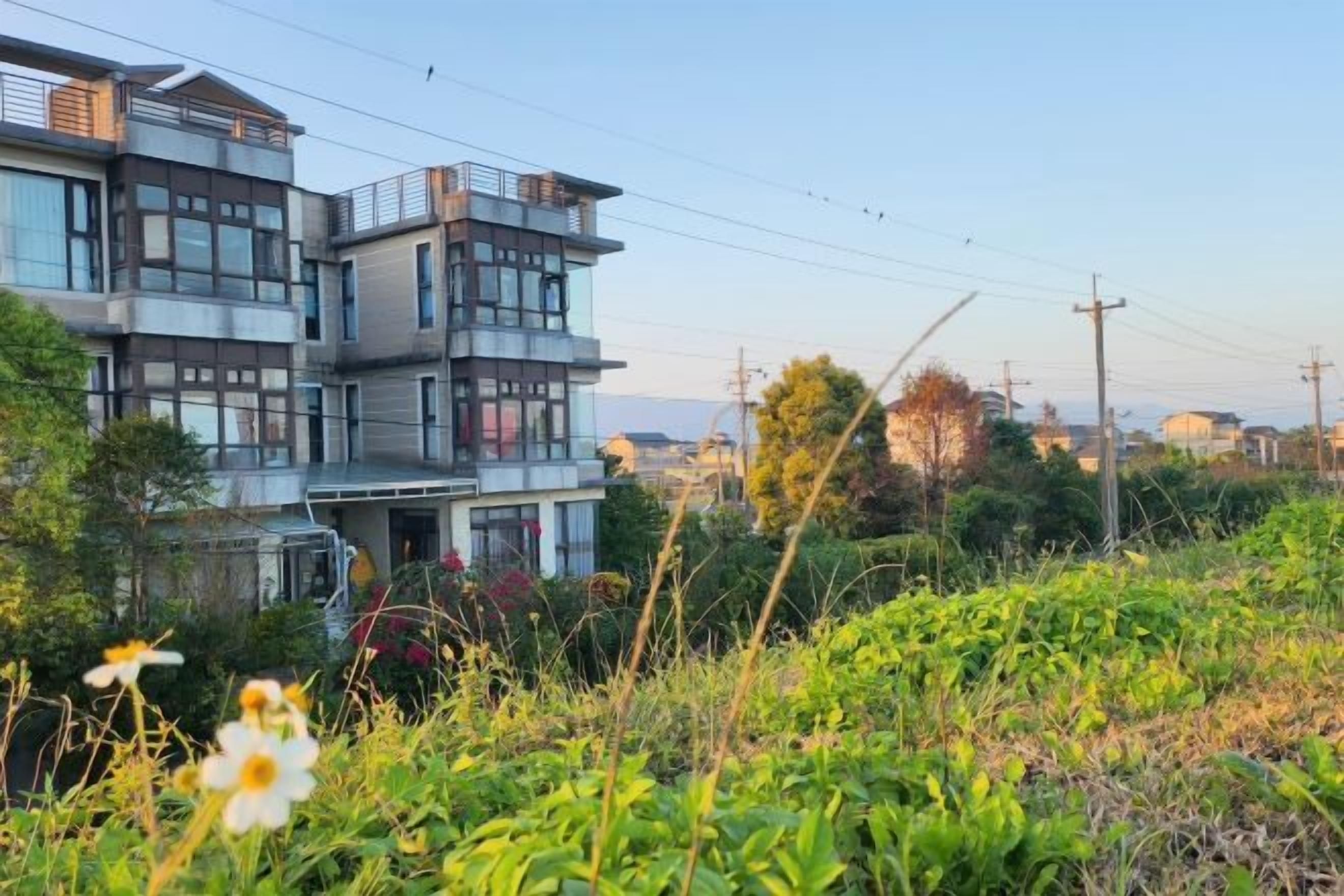 A multi-story residential building with a modern architectural style, surrounded by lush greenery and a clear sky.