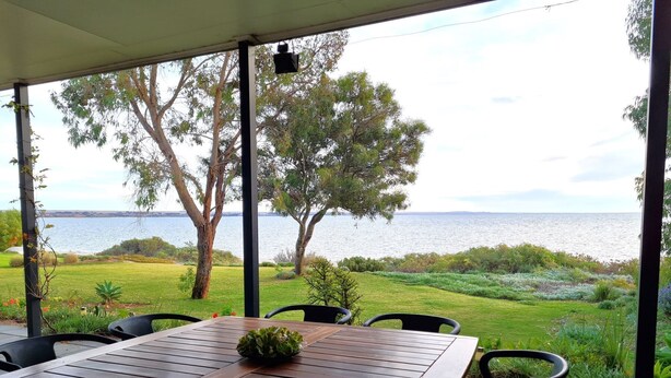 A covered outdoor seating area with a wooden table and chairs, overlooking a grassy landscape and a body of water. - Reads Retreat, Black Point (Black Point)
