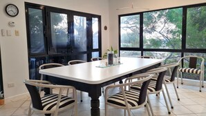 A dining area with a large table and six chairs, large windows with a view of trees, a ceiling fan, and a wall clock. - Reads Retreat, Black Point (Black Point)