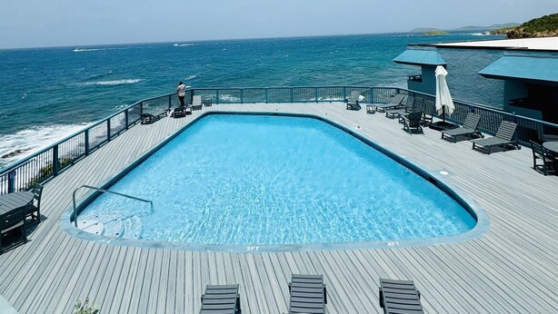A pool with a wooden deck, lounge chairs, and a view of the ocean. - Sea You Soon Retreat+Jeep option (St. Thomas)