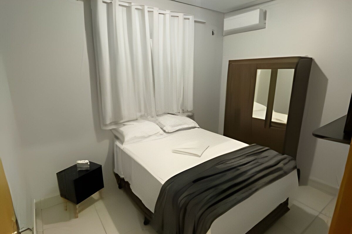 Un dormitorio con cama, mesita de noche, armario y lámpara en el techo.