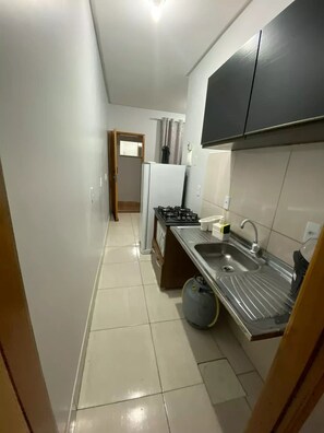A compact kitchen with a gas stove, sink, and cabinets. - EDIFICIO GERVASIO (Goiania)