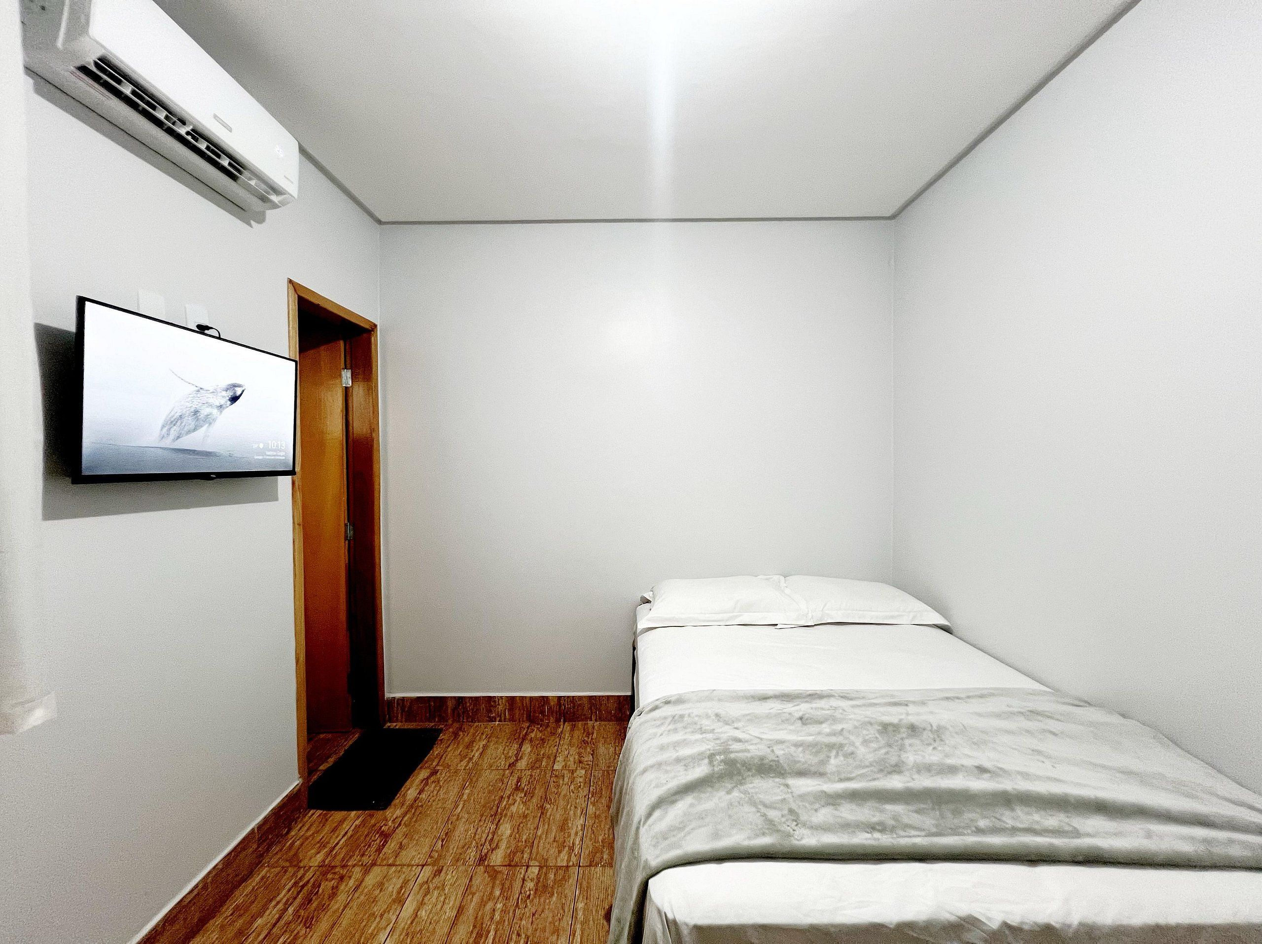Una habitación pequeña y poco amoblada, con una cama individual, una puerta de madera y un televisor montado que muestra un pájaro.