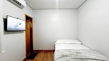 Una habitación pequeña y poco amoblada, con una cama individual, una puerta de madera y un televisor montado que muestra un pájaro.