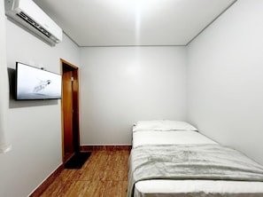 Una habitación pequeña y poco amoblada, con una cama individual, una puerta de madera y un televisor montado que muestra un pájaro.