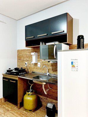 A compact kitchen with a gas stove, sink, and a small refrigerator. - EDIFICIO GERVASIO (Goiania)