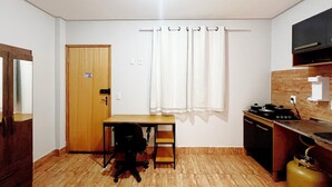 Une petite pièce, de taille modeste, avec une porte en bois, une petite table et une chaise, un réchaud à gaz et un évier.