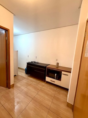 A compact kitchen with a gas stove, microwave, and a small countertop. - EDIFICIO GERVASIO (Goiania)