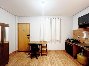 A small, compact room with a wooden door, a small table with a chair, a gas stove, and a sink. - EDIFICIO GERVASIO (Goiania)