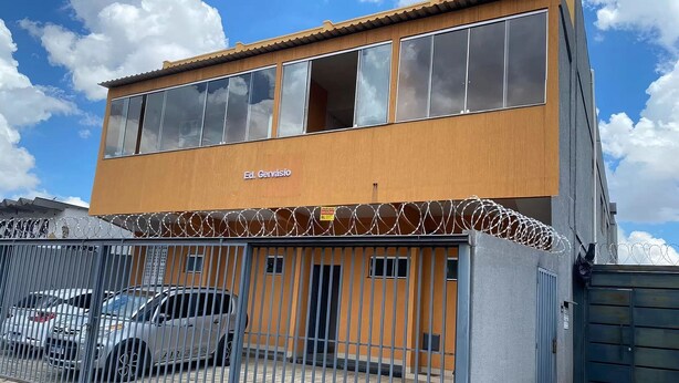 Un bâtiment à deux étages, sur lequel on peut lire l’inscription « Ed. Gervásio », et un espace de stationnement clôturé où sont garées plusieurs voitures.