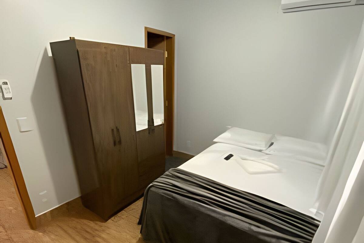 A bedroom with a bed, a wardrobe, and an air conditioning unit.