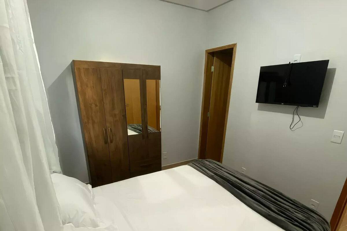 A bedroom with a bed, a wardrobe, a television mounted on the wall, and a door.