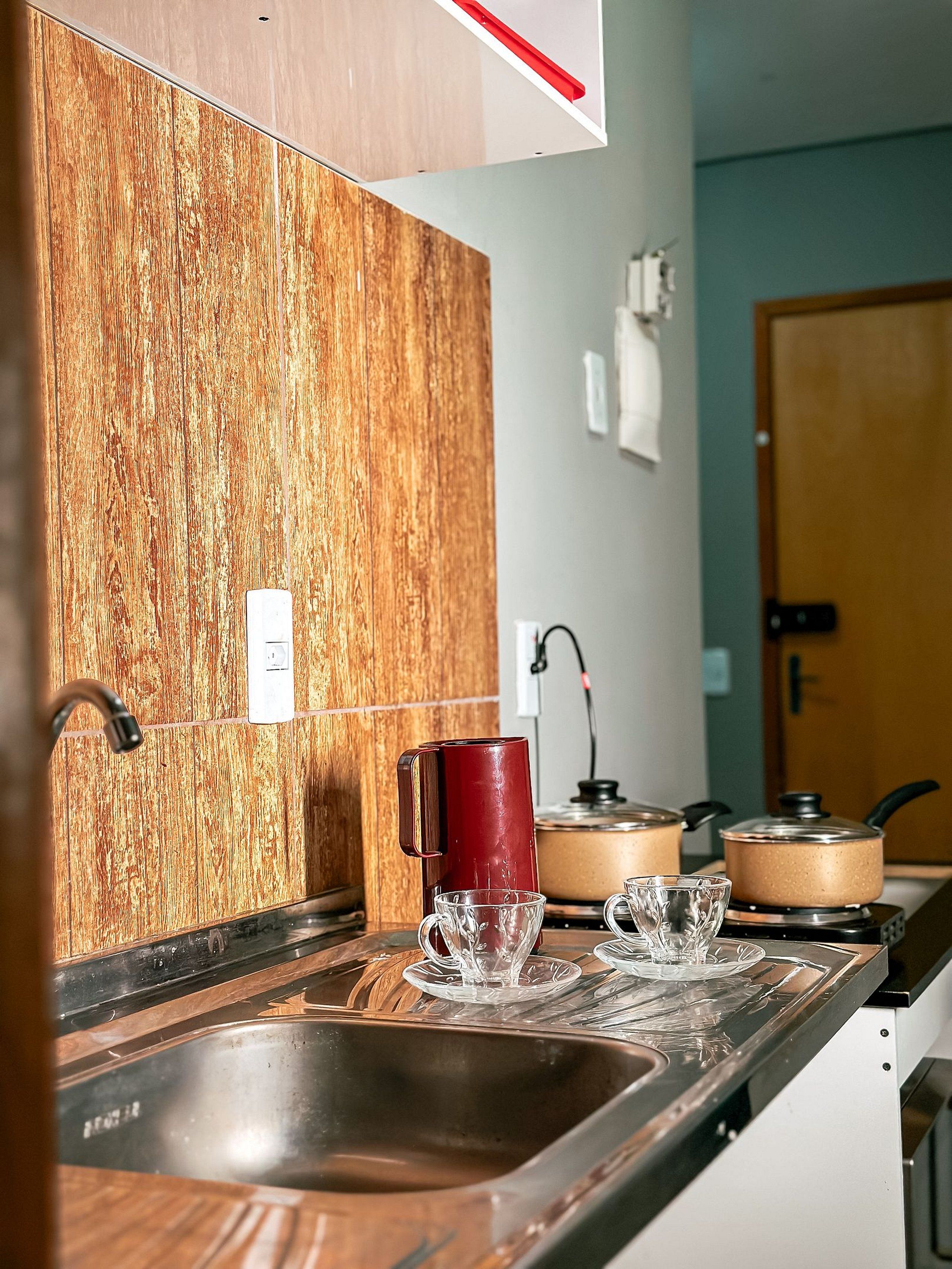 A kitchen with wooden backsplash, stainless steel sink, and two electric kettons on the stove.