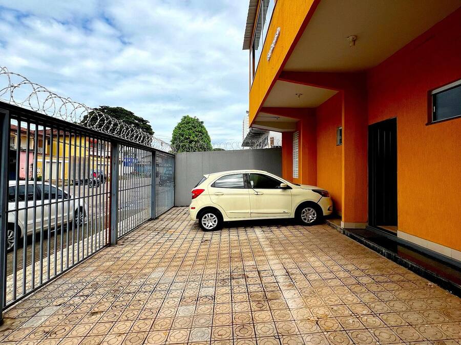 Um carro estacionado numa área de estacionamento coberta, com chão de azulejos e uma vedação metálica com arame farpado.