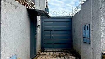Un estrecho callejón con una puerta azul, suelo de baldosas y alambre de púas en las paredes.
