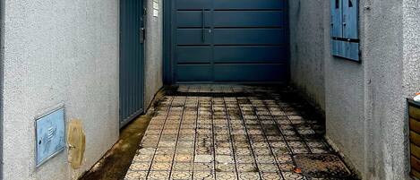 A narrow alleyway with a blue gate, tiled floor, and barbed wire on the walls.