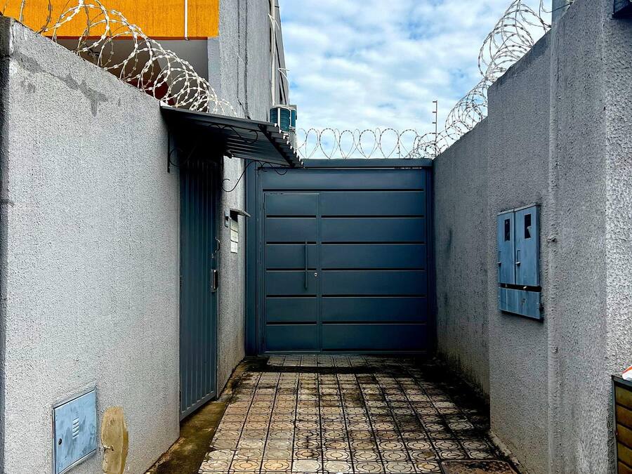 Une ruelle étroite avec une porte bleue, un sol carrelé et du fil de fer barbelé sur les murs.
