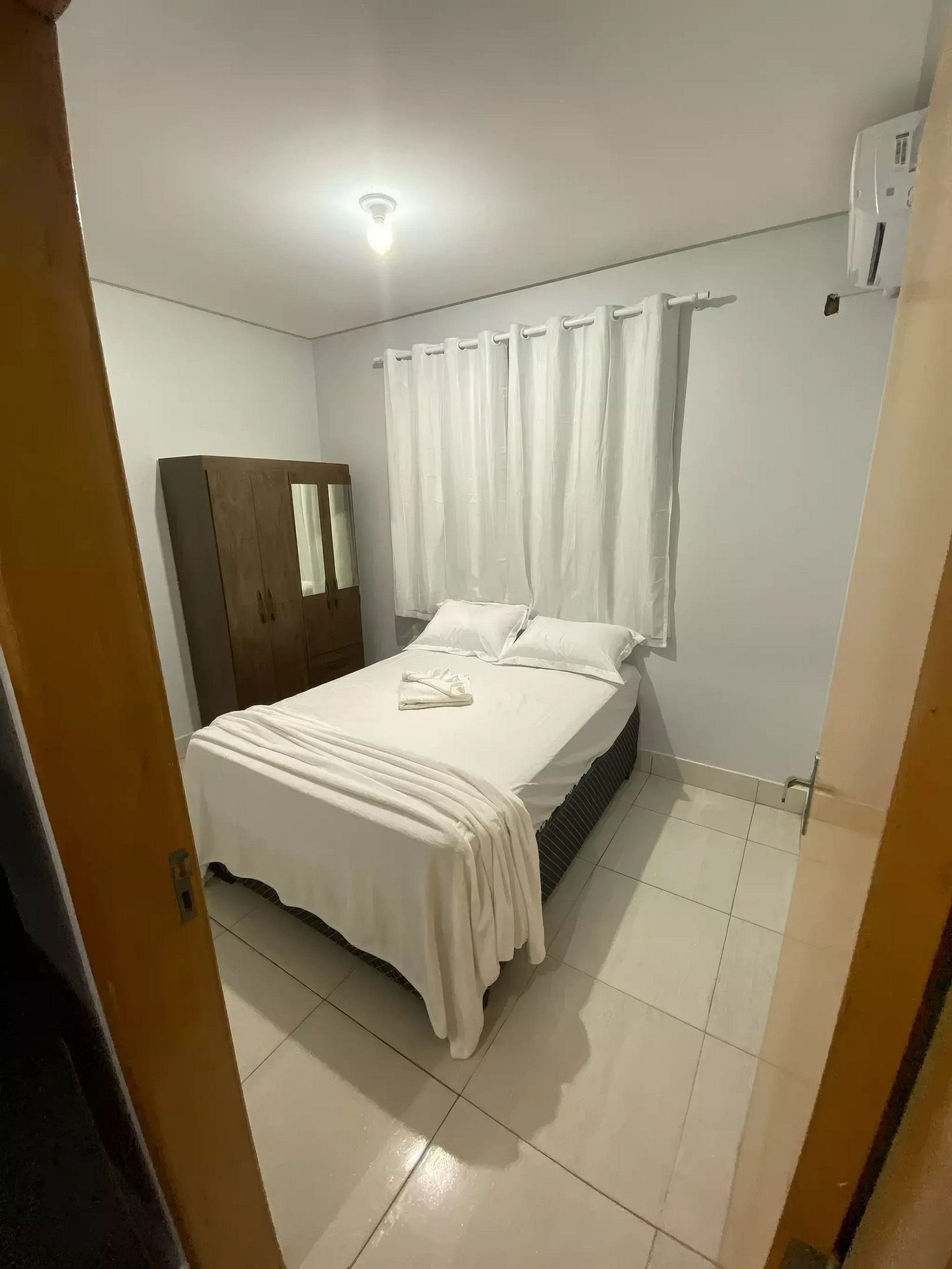 A bedroom with a bed, a wardrobe, a window with curtains, and a ceiling light.