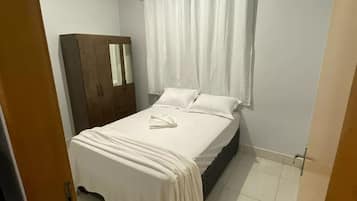 A bedroom with a bed, a wardrobe, a window with curtains, and a ceiling light.