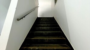 Un escalier aux murs blancs et à la rampe métallique, menant à un palier doté d’une fenêtre.