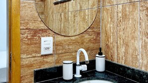 Une salle de bain avec un mur en bois, un miroir rond, un lavabo blanc et un robinet.