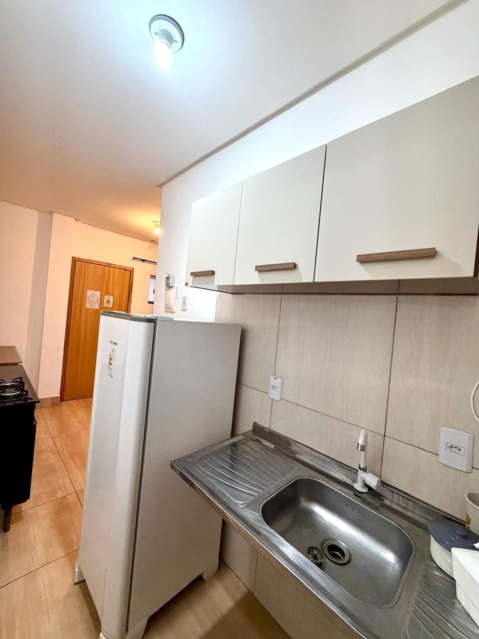 Una cocina compacta con armarios blancos, un lavamanos de acero inoxidable y un refrigerador empotrado.