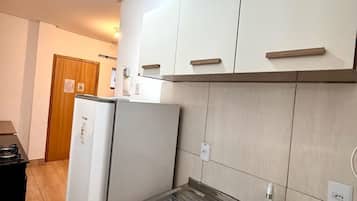 Una cocina compacta con armarios blancos, un lavamanos de acero inoxidable y un refrigerador empotrado.