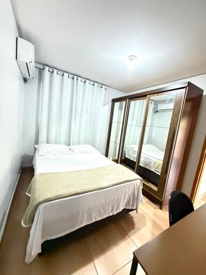 A hotel room with a bed, a desk, a wardrobe, and an air conditioning unit. - EDIFICIO GERVASIO (Goiania)