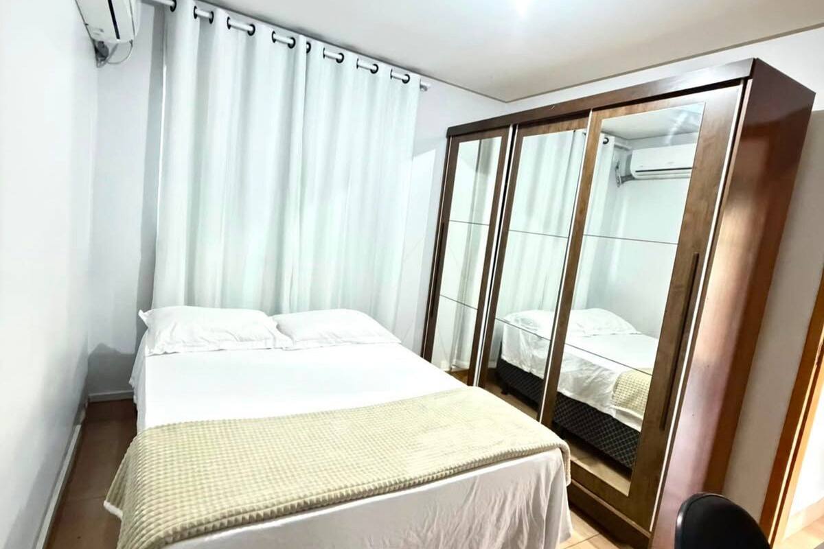 A hotel room with a bed, a desk, a wardrobe, and an air conditioning unit.