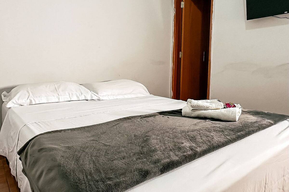 A hotel room with a bed, a television mounted on the wall, and a wooden door.
