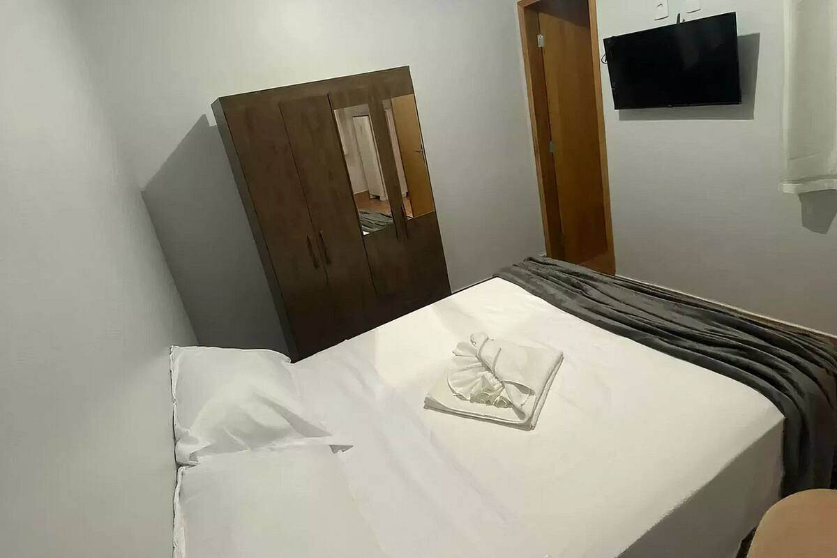 A bedroom with a bed, a wardrobe, a TV, and an air conditioning unit.
