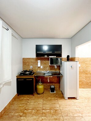 A compact kitchen with a gas stove, microwave, and refrigerator. - EDIFICIO GERVASIO (Goiania)