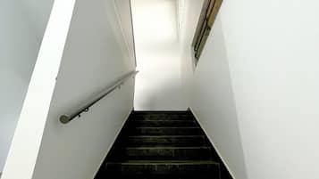 A staircase with white walls and a metal handrail, leading to a landing with a window.
