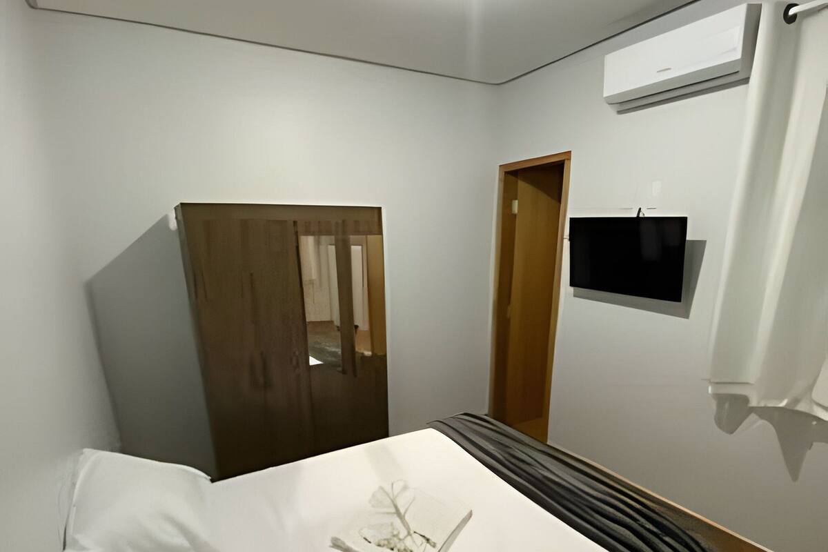 A bedroom with a bed, a wardrobe, a TV, and an air conditioning unit.