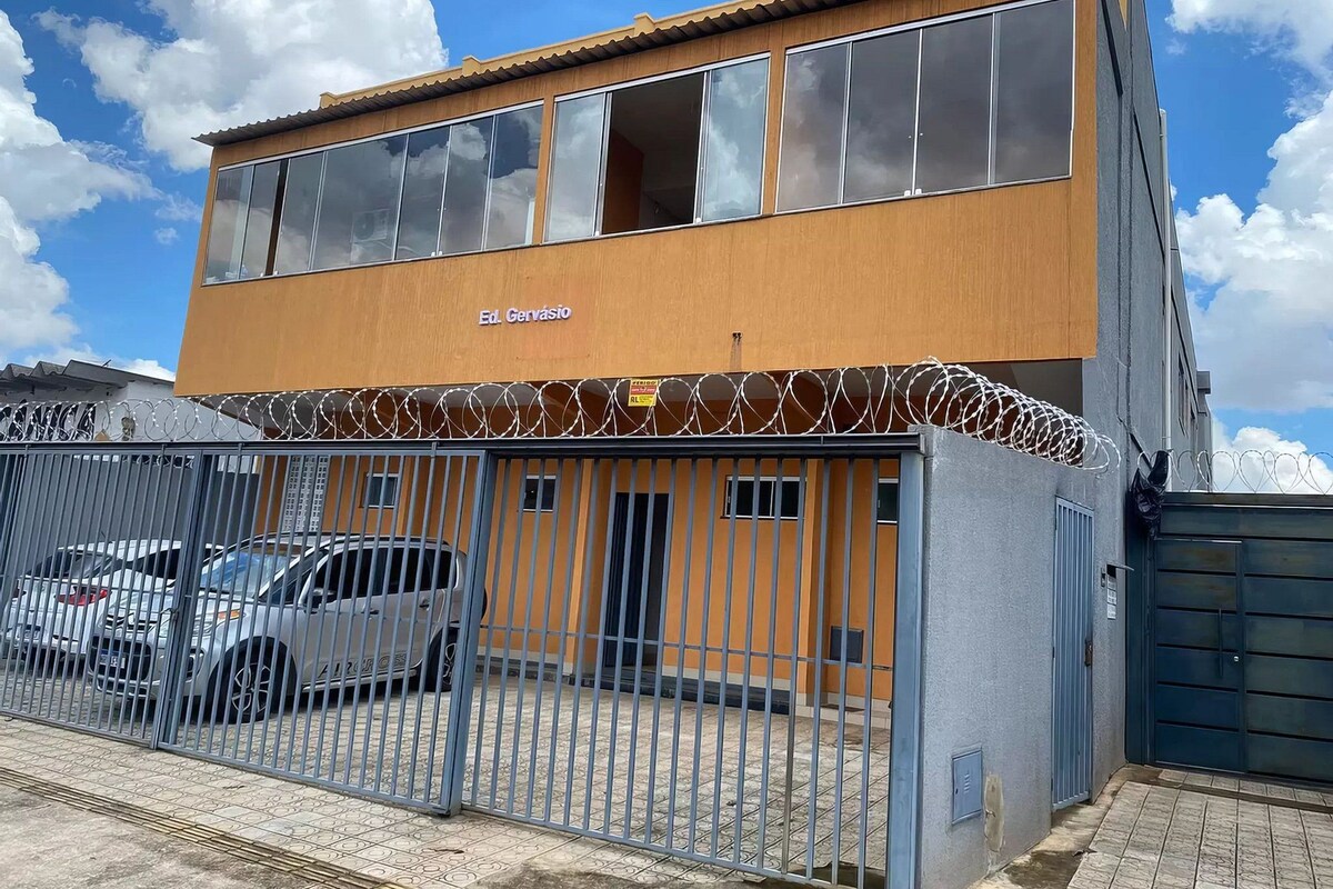 A two-story building with a sign reading "Ed. Gervásio" and a fenced parking area with several cars.