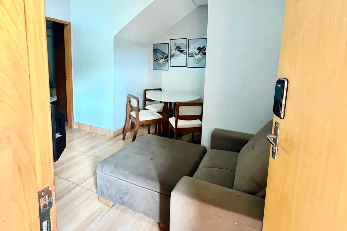 A loft-style living space with a high ceiling, a sectional sofa, a dining table with chairs, and a wall-mounted artwork.