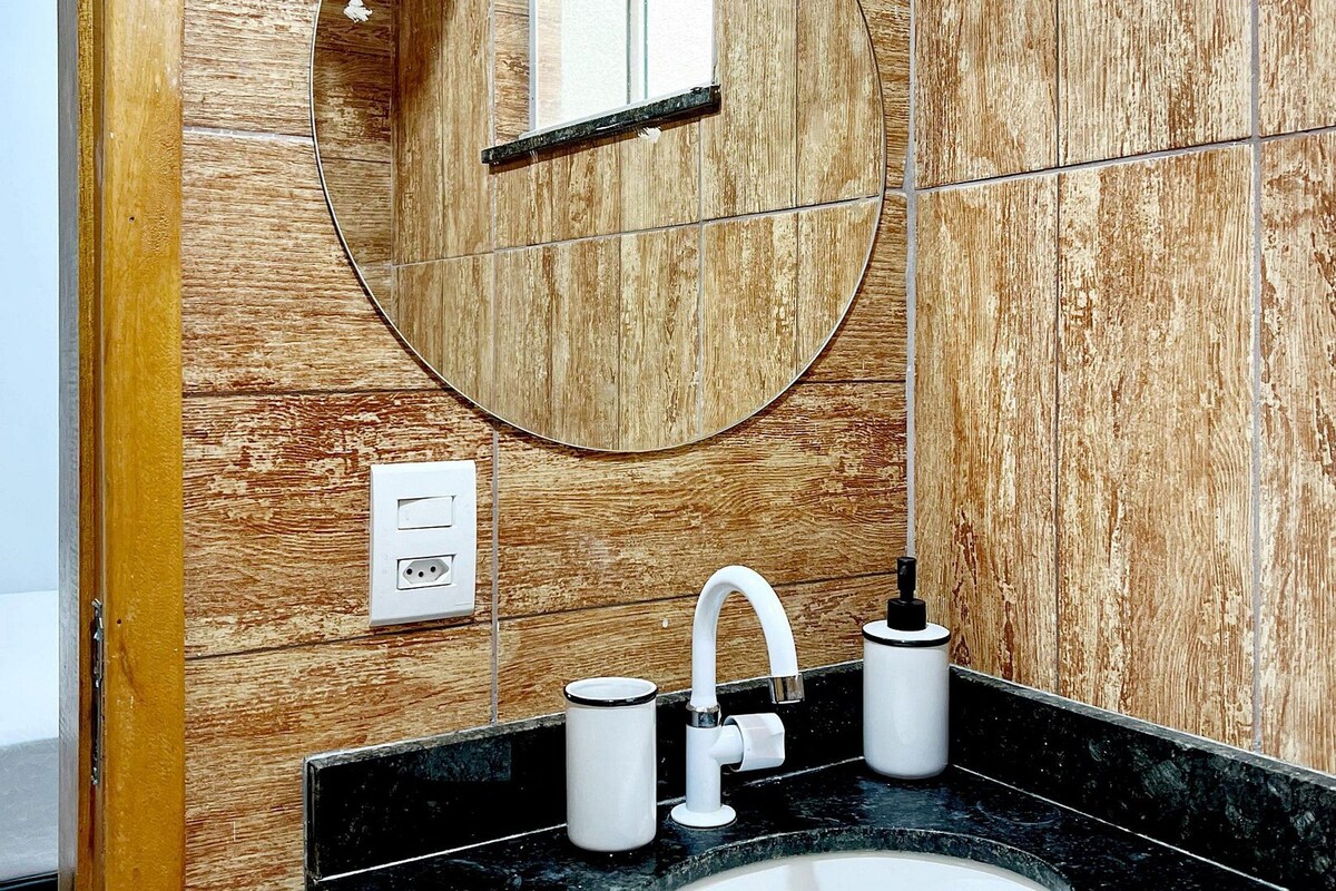 A bathroom with a wooden wall, a round mirror, a white sink, and a faucet.
