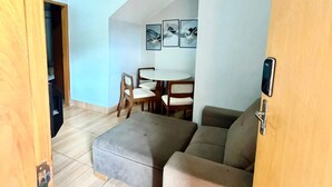 Un espace de vie de style loft avec un plafond haut, un canapé d’angle, une table à manger avec des chaises et une œuvre d’art accrochée au mur.