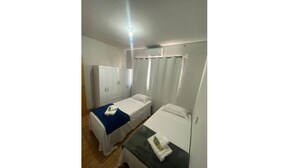 Une chambre avec deux lits simples, une armoire, une table et un luminaire au plafond.