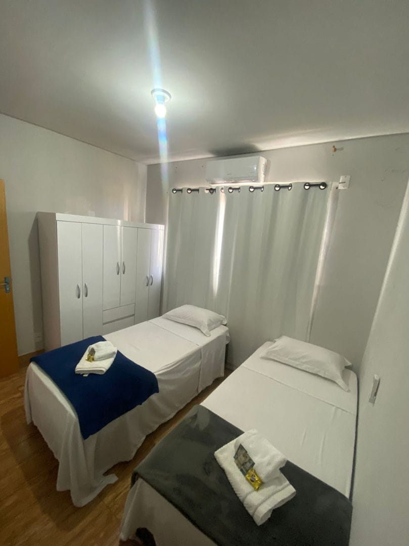 Una habitación con dos camas individuales, un armario, una mesa y una lámpara en el techo.