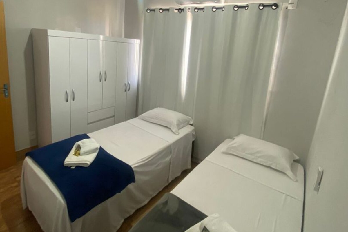 A room with two single beds, a wardrobe, a table, and a ceiling light.