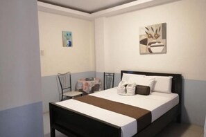 A bedroom with a bed, a chair, a table with a tablecloth, and two wall-mounted artworks. - RedDoorz @ Bansud Oriental Mindoro (Bansud)