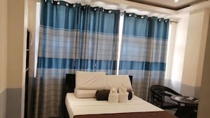 A hotel room with a bed, a chair, a small table, and curtains. - RedDoorz @ Bansud Oriental Mindoro (Bansud)