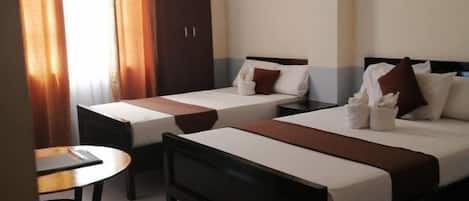 A hotel room with two beds, a small table, and a wardrobe.
