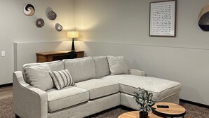 Ein modernes Wohnzimmer mit einem Ecksofa, zwei runden Tischen, einer Lampe und Wanddekoration.