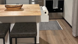 Eine kompakte Küche mit integriertem Mikrowellenherd, Herd und Spüle. Auf der Arbeitsfläche steht eine Holzkugel und es gibt eine kleine Kücheninsel mit Hockern.