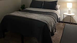 Ein Schlafzimmer mit einem Bett, einem Nachttisch mit Lampe, einem Bild an der Wand und einer Deckenleuchte.